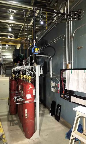 Industrial pipes and valves lined up in a factory setting with control panels.